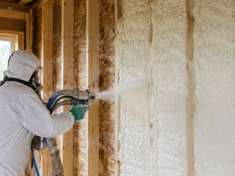 A Cape Breton Spray Foam Insulation installer spraying a framed wall in full protective kit