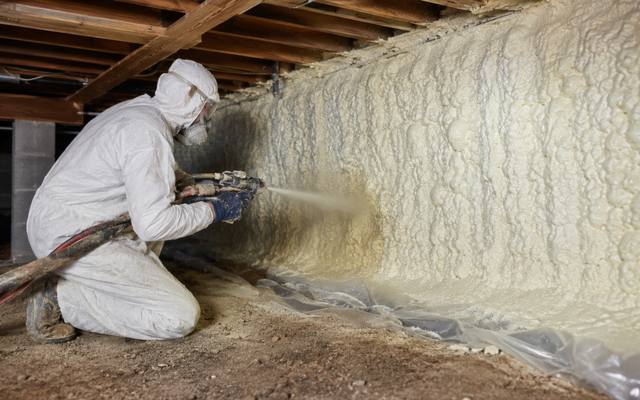 Installer sealing a foundation wall over a taped ground sheet in full protective kit